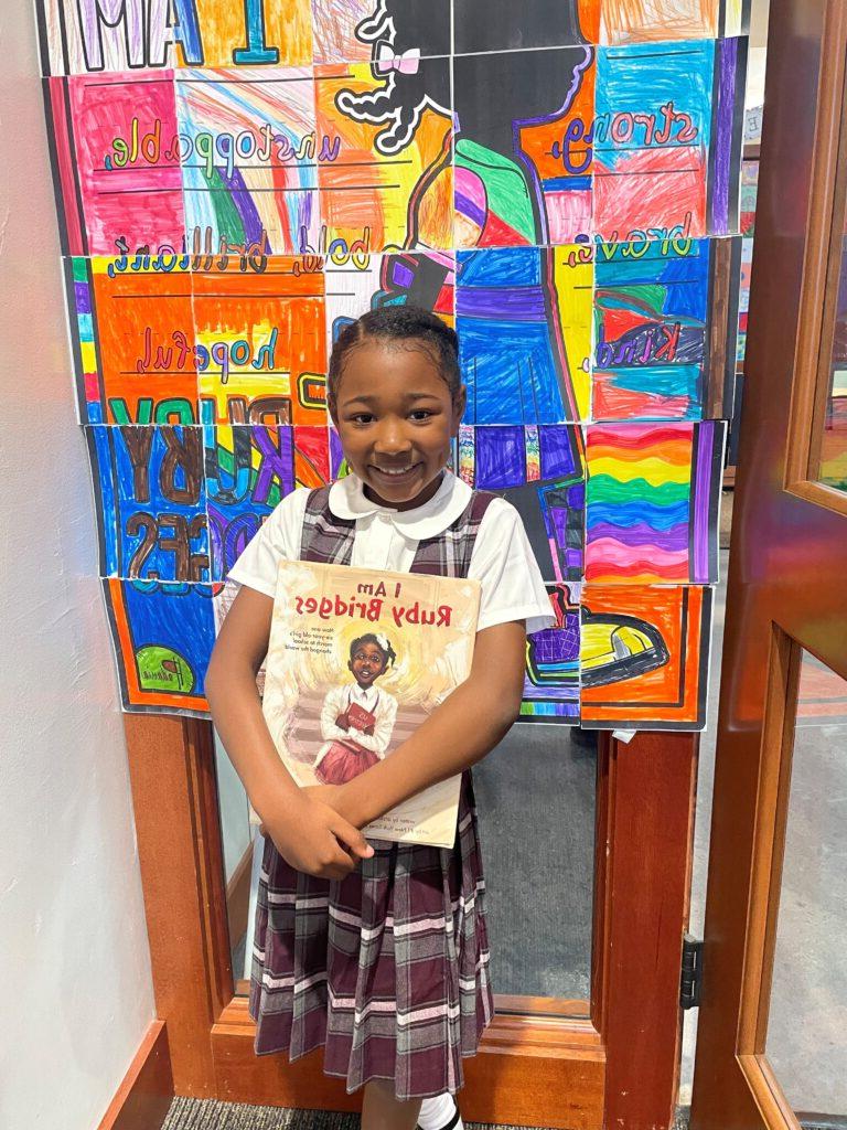 Student dressed as Ruby Bridges poses in front of ruby bridges student art wall.